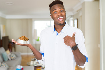 Sticker - African american man holding metal bowl with cat or dog dry food with surprise face pointing finger to himself