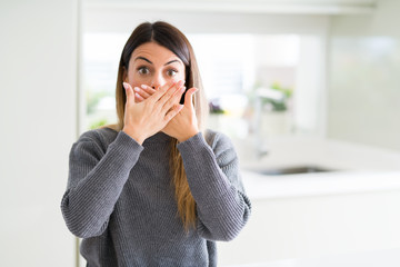 Wall Mural - Young beautiful woman wearing winter sweater at home shocked covering mouth with hands for mistake. Secret concept.