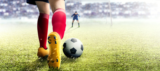 Football player woman in orange jersey kicking the ball in the penalty box