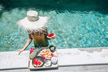 Wall Mural - Girl eating fruits in pool on luxury villa in Bali