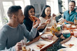 © gstockstudio - Dinner with friends. Group of young people in casual wear eating pizza and smiling while having a dinner party indoors