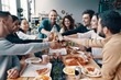 © gstockstudio - Cheers to friends! Group of young people in casual wear toasting each other and smiling while having a dinner party indoors