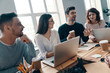 © gstockstudio - Happy business partners. Group of young modern people in smart casual wear discussing something and smiling while working in the creative office
