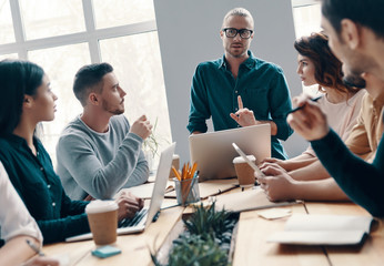 Wall Mural - Developing new project. Group of young modern people in smart casual wear discussing something while working in the creative office