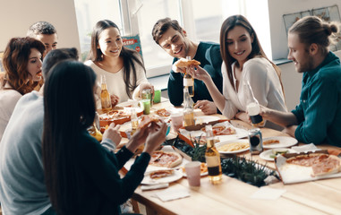 Unforgettable party. Group of young people in casual wear eating pizza and smiling while having a dinner party indoors