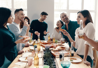 Sticker - Great party. Group of young people in casual wear eating pizza and smiling while having a dinner party indoors