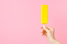 Young Woman Hand Holding Bright Yellow Ice Cream With Lemon Glaze On Pastel Pink Background. Empty Place For Text, Quote Or Sayings. Front View. 