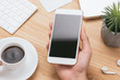 © makistock - Male hands holding white phone with blank screen on the men table