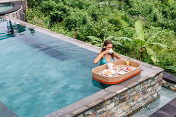 Wall Mural - Girl eating floating breakfast in luxury hotel pool