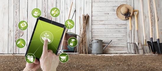 gardening equipment e-commerce concept, online shopping on digital tablet, hand pointing and touch screen with garden tools icons, tool shed in the background