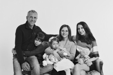 group of people on a white background: adults and children with toys sitting on the same couch