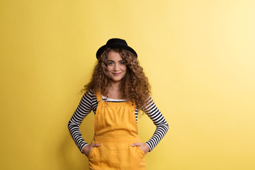 Wall Mural - Portrait of a young woman with black hat in a studio on a yellow background.