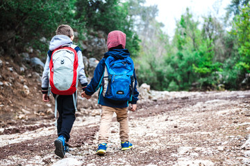 Two boys with backpacks are walking along a forest path.