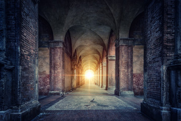 rays of divine light illuminate old arches and columns of ancient buildings. bologna, italy. concept
