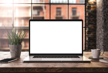 Laptop with blank screen mockup template on table in industrial old factory loft interior - front view
