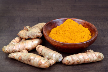 Organic healthy Turmeric powder in a bowl with Turmeric roots on wooden background