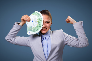 Excited young business woman with fan of 100 euro bills  in a studio on a blue background