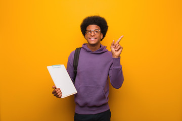 Wall Mural - Young african american student man holding a clipboard pointing to the side with finger