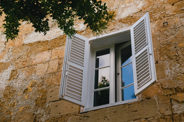 Typical traditional window with white wooden blind at narrow medieval street in Mdina, ancient capital of Malta, fortified medieval town. Popular touristic destination and attraction