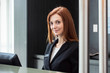 © PhotoAlto - Portrait of smiling female receptionist standing at hotel reception desk