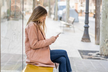 Young Woman With Cell Phone Waiting At Bus Stop