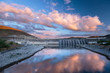 © Tandem Stock - Grand Coulee Dam in central Washington State under a colorful sunset. The dam is the largest capacity power station in the U.S.  The nearby Franklin Delano Roosevelt Reservoir provides water for the irrigation of 670,000 acres of farmland in the Columbia Basin. 3,000 people were forced to relocate before construction and numerous First Nation ancestral land sites were flooded. The monumental project was one of a variety of FDR era New Deal projects.