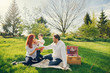 © prostooleh - beautiful and stylish redhead mom in a white blouse sits on the grass with her beautiful man dressed in a white shirt and blue jeans; they play with their little sweet son who eats grapes