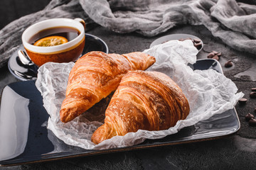 Wall Mural - Breakfast with fresh french chocolate croissants on paper over dark background with napkin and cup of tea. Dessert, puff pastries, top view