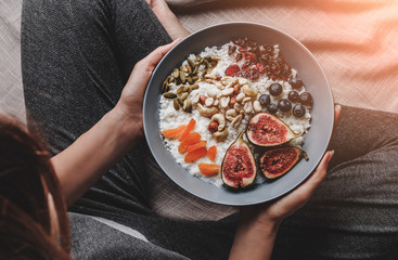 Woman in home clothes eating vegan Rice coconut porridge with figs, berries, nuts. Healthy breakfast ingredients. Clean eating, vegan food concept, toning