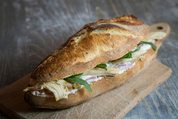 Sticker - Chicken  with cream cheese in a French baguette, with some slices of rucola salad and chicken dressing on a rustic wooden table. This sandwich, in France, is called sandwich au poulet
