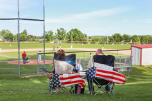 Parents Sitting In Folding Chairs Watching A High School Baseball Game
