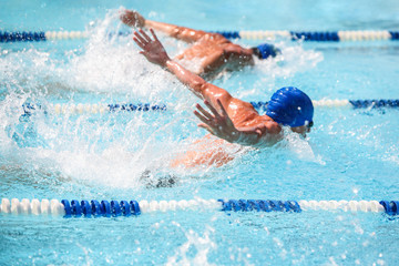 Sticker - Men swimming butterfly stroke in a race, focus on water droplets,  swimmer is out of focus