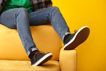 Stylish man in shoes sitting on armchair against color background