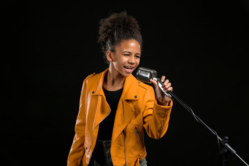 Wall Mural - African-American girl with microphone singing against dark background