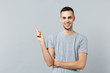 Portrait of smiling young man in casual clothes looking camera, pointing index finger aside isolated on grey wall background in studio. People sincere emotions, lifestyle concept. Mock up copy space.