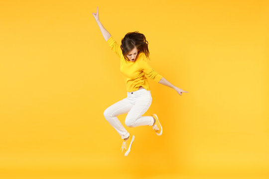 Cheerful funny young woman in summer casual clothes jumping and spreading hands isolated on yellow orange wall background in studio. People sincere emotions, lifestyle concept. Mock up copy space.