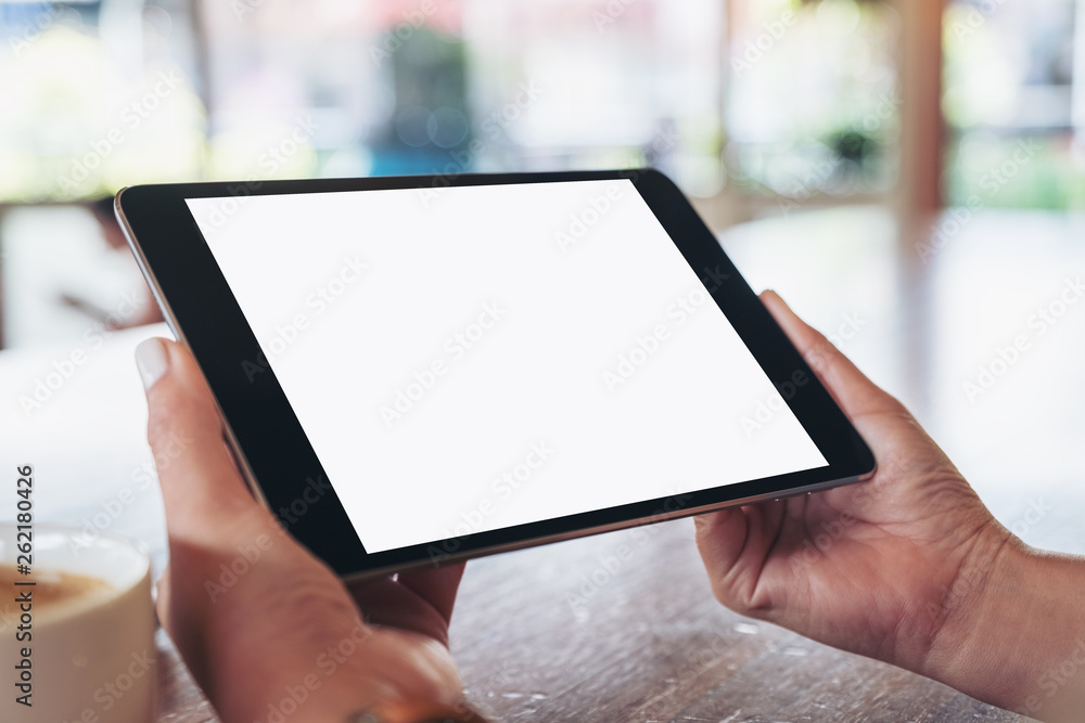 Mockup image of hands holding black tablet pc with blank white screen horizontally with coffee cup on wooden table - obrazy, fototapety, plakaty 