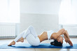 © vitaliymateha - young sporty woman in white sportswear doing yoga or pilates exercise in yoga studio with white wall background. Athletic lady doing variation of Matsyasana, Fish pose with crossed arms and legs