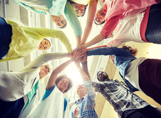 Poster - education, school, teamwork and people concept - group of international students with hands on top of each other over table