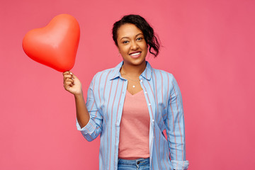 Wall Mural - valentine's day and people concept - happy african american young woman with red heart-shaped balloon over pink background