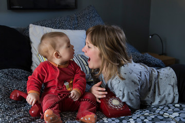 pretty little girl lying on bed laughing out loud and her cute chubby baby sister in pyjamas sitting