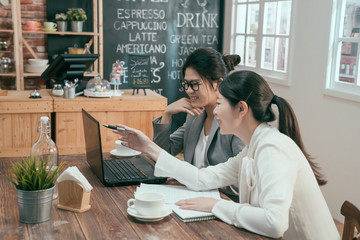 Wall Mural - young asian businesswomen at cafe shop with laptop discussing work and smiling. business professionals office ladies colleagues having casual discussing overwork at coffee bar after work point screen