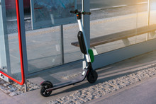 Electric Scooter Stands Near Public Bus Stop. Electric Scooters Stand Along The Streets Of Downtown. The Public Scooters Are Available To Rent As A Means Of Transportation Throughout The City