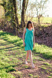© Tetiana Soares - Beautiful preteen romantic girl in turquoise dress walking barefoot on dirt road with green grass at warm sunny spring or summer day. Vacation in village
