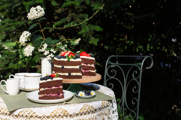 Sticker - Slice of layered chocolate cake decorated with flowers and berries on the garden table.