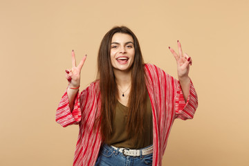 Portrait of cheerful young woman in casual clothes looking camera, showing victory sign isolated on pastel beige background in studio. People sincere emotions, lifestyle concept. Mock up copy space.