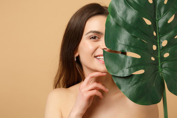 Wall Mural - Close up brunette half naked woman 20s with perfect skin, nude make up palm leaf isolated on beige pastel wall background, studio portrait. Health care cosmetic procedures concept. Mock up copy space.