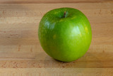 Fototapeta  - Single isolated green apple on a wooden board