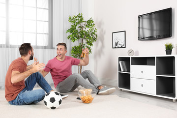 Wall Mural - Young men watching TV while sitting on floor at home. Sport channel