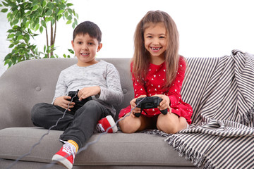 Sticker - Cute children playing video game on sofa in living room